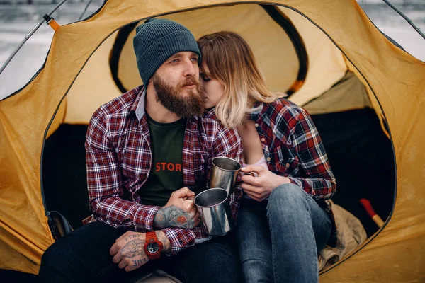Jeune couple assis dans une tente et boit du thé chaud pendant la randonnée hivernale . — Photo