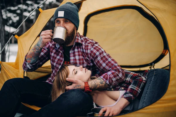 Jovem casal em tenda turística durante a caminhada de inverno. Guy bebe quente — Fotografia de Stock