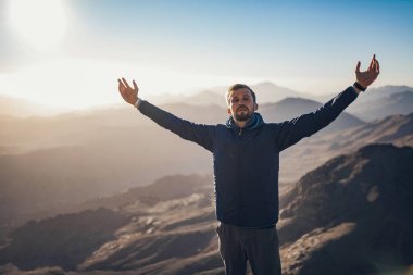 Adam standları basma çerçevede gündoğumu dağlarında kolları ile.