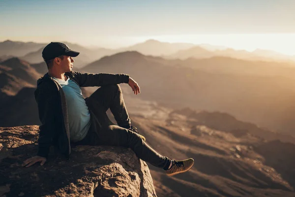 Man zit op de rand van de klif op de berg Sinaï en kijkt bij zonsopgang. — Stockfoto