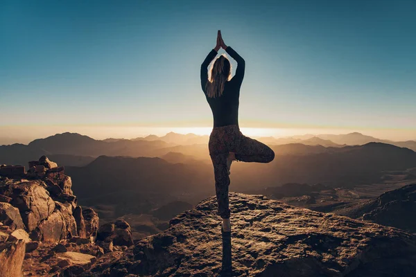 妇女做瑜伽演习在西奈山上的悬崖上的背景日出. — 图库照片