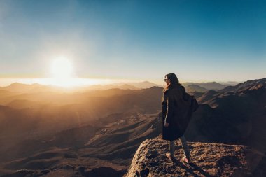 Kadın gündoğumu çerçevede Sina Dağı üzerinde uçurumun kenarında duruyor.
