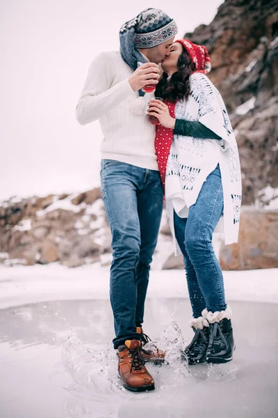 Junges Paar mit heißem Tee in der Hand küsst und steht in einer Pfütze aus geschmolzenem Wasser. — Stockfoto
