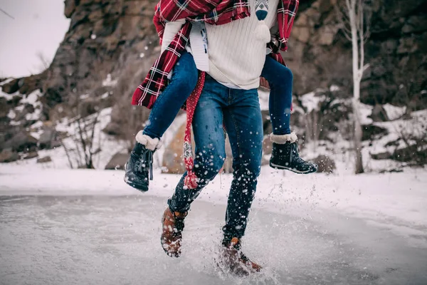 Junger Mann trägt seine Freundin auf Rücken über Pfütze aus geschmolzenem Wasser mit Spritzern . — Stockfoto