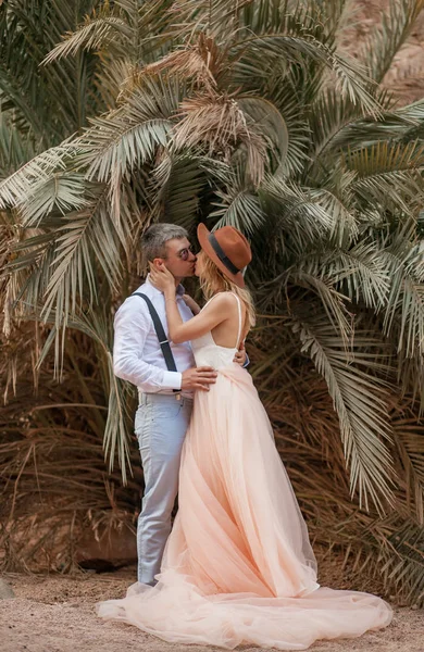 Pie de novia y novio, abrazo y beso en el fondo de palmeras . — Foto de Stock