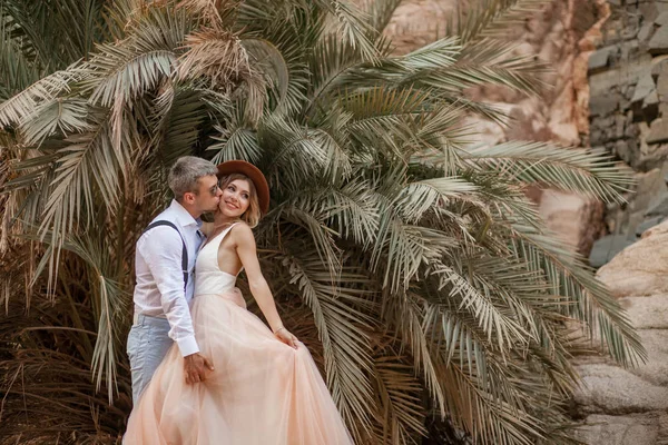 Abrazos de novio y besos de novia en el fondo de palmeras y rocas . — Foto de Stock