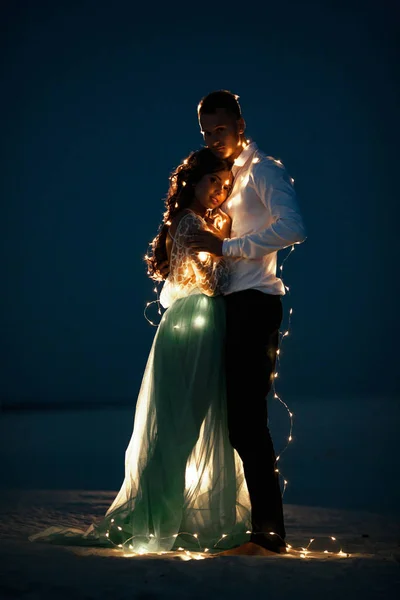 新郎新婦のスタンドとの抱擁砂漠次に電球のガーランドに夜. — ストック写真