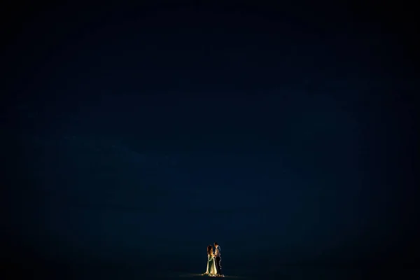 Nevěsta a ženich stojan a držte ruce v poušti se věnec žárovky v noci. — Stock fotografie