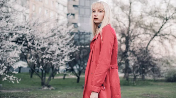 Mujer rubia joven va a caminar en el jardín de primavera en el fondo de los árboles en flor . —  Fotos de Stock