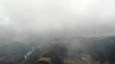 Karpat dağlarındaki sislerin arasından insansız hava aracından ormana, nehre ve köye güzel bir manzara. 