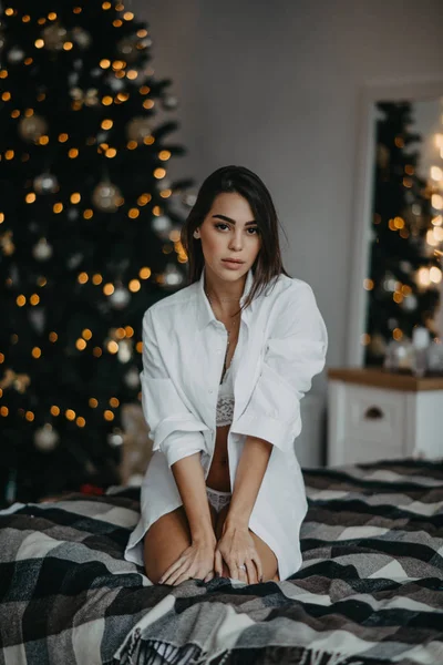 Giovane donna si siede sul letto sullo sfondo dell'albero di Natale — Foto Stock