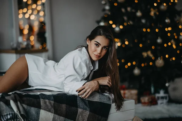 Jovem deita-se na cama contra o fundo da árvore de Natal — Fotografia de Stock