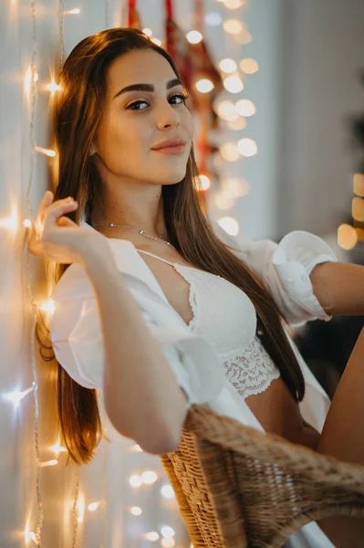 Jovem mulher senta-se na poltrona e sorri contra a árvore de Natal — Fotografia de Stock