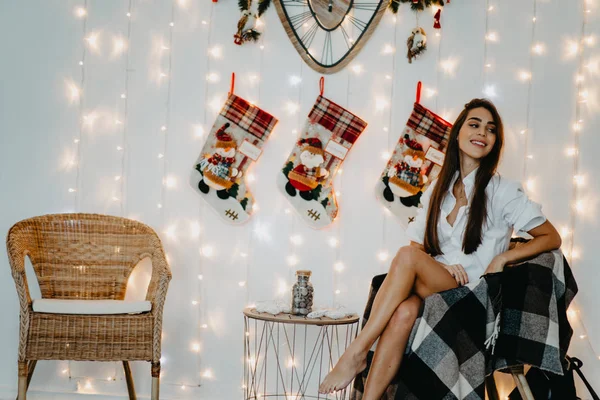 Jovem mulher senta-se na poltrona e sorri contra decorações de Natal . — Fotografia de Stock
