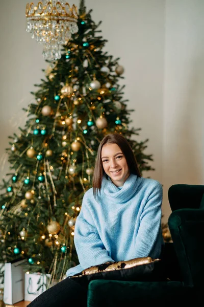 Mutlu kadın Noel ağacının arka planında oturur. — Stok fotoğraf