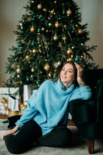 문신을 한 행복 한 여인 이 크리스마스 트리의 배경에 앉아 있다 — 스톡 사진