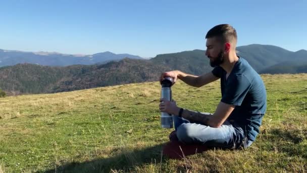 Giovane Uomo Siede Prato Montagna Versa Beve Thermos Guarda Montagne — Video Stock