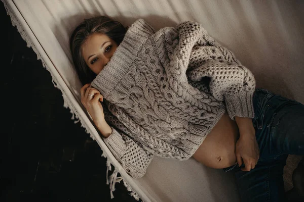 Těhotná žena v svetru a džíny spočívá v houpací síti. — Stock fotografie