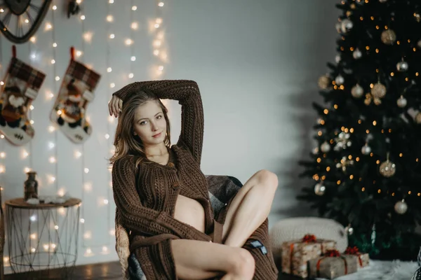 Mujer embarazada se sienta en sillón contra el fondo del árbol de Navidad — Foto de Stock