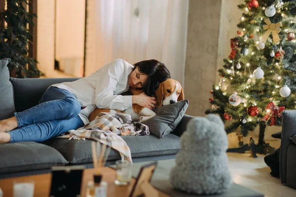 Женщина лежит рядом с собакой и обнимает его на фоне рождественской елки . — стоковое фото