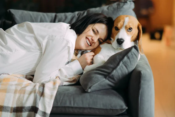 A woman lies next to a dog and hugs him.