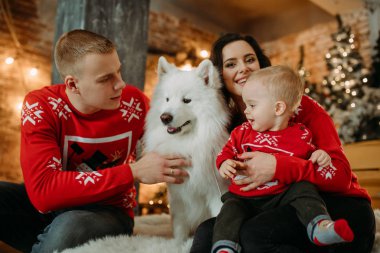 Aile köpeğin yanına oturur ve bir Noel ağacının arka planına karşı eğlenir.