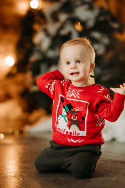 Küçük çocuk Noel ağacının arka planında oturuyor.