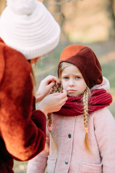 Mother puts on beret on her daughter, the girl is unhappy. — 스톡 사진
