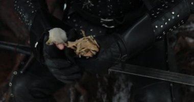 Cosplayer ortaçağ savaşçısı karakterini canlandırıyor ve kış ormanlarında kuru çimlerle kılıcını temizliyor..