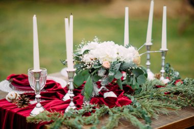 Şamdanlarda mumlar, tabaklar, şarap bardakları, çiçek aranjmanı ve kırmızı masa örtüsü olan düğün masası. Yakın çekim..