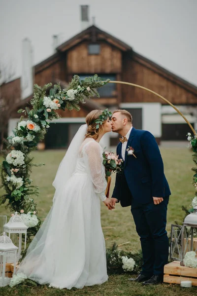 Nygifta Står Bakgrunden Bröllopsbågen Håller Varandras Händer Och Kysser Varandra — Stockfoto