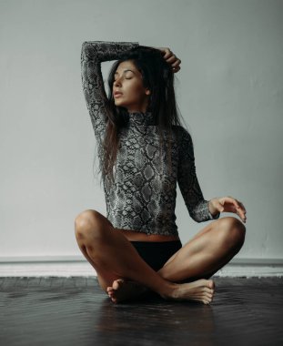 Stüdyoda poz veren genç bir kadın yerde oturuyor..