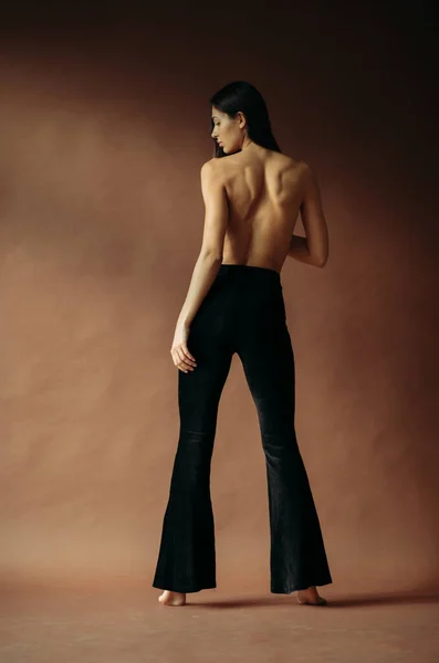 Young woman in pants posing with a bare back in the studio.