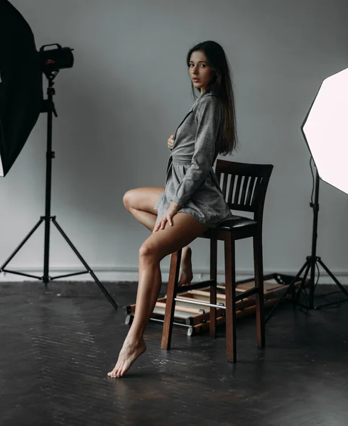 在照相馆里摆姿势的年轻女子坐在灯具旁边的椅子上 — 图库照片