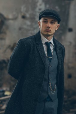 1920 'lerin eski bir gangsteri gibi poz veren bir adam. Palto, takım elbise ve düz şapka giymiş Peaky at gözlüğü tarzında..