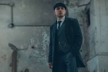 1920 'lerin eski bir gangsteri gibi poz veren bir adam. Palto, takım elbise ve düz şapka giymiş Peaky at gözlüğü tarzında..
