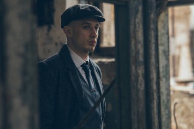 1920 'lerin eski bir gangsteri gibi poz veren bir adam. Palto, takım elbise ve düz şapka giymiş Peaky at gözlüğü tarzında..