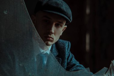 1920 'lerin Peaky at gözlüğü tarzında giyinmiş eski bir İngiliz gangsterinin portresi. Kırık camlardan bak.
