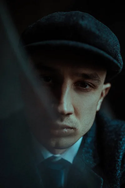Portrait of a man in the image of an English retro gangster of the 1920s dressed in Peaky blinders style. View through broken glass.