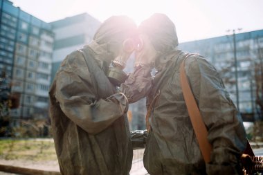 Couple in love hugs in NBC protective suits and gas masks. Concept of a preventive measures and protection for coronavirus COVID 19 pandemic and other global dangers. Backlight. clipart