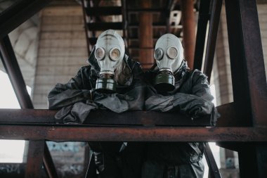 Birbirine aşık bir çift, NBC koruyucu giysileri ve gaz maskeleriyle köprünün altında duruyor. Koronavirüs COVID için önleyici önlemler ve koruma kavramı 19 salgın hastalık ve diğer küresel tehlikeler.