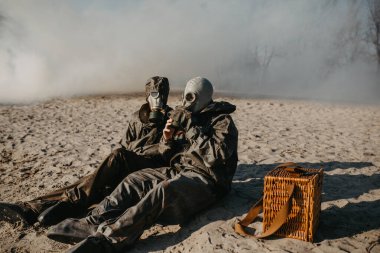 Birbirine aşık çiftler NBC 'nin koruyucu giysileri ve gaz maskeleriyle arka planda otururlar. Kıyametin önleyici tedbirleri ve korunması kavramı, küresel çevre kirliliği ve salgın hastalık.