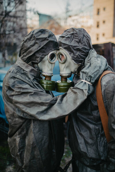 Couple in love hugs in NBC protective suits and gas masks. Concept of a preventive measures and protection for coronavirus COVID 19 pandemic and other global dangers.