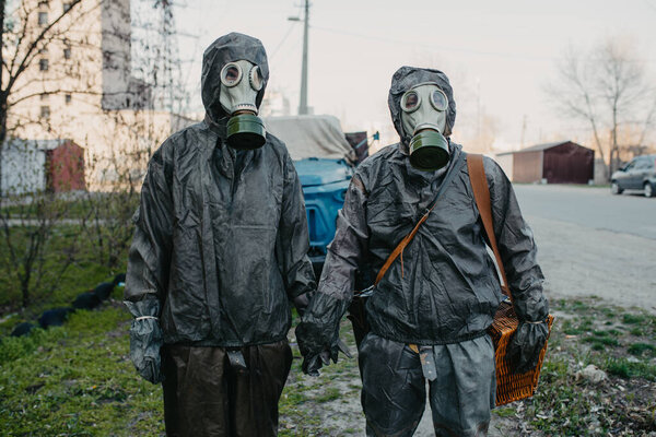 Couple in love holds hands in NBC protective suits and gas masks. Concept of a preventive measures and protection for coronavirus COVID 19 pandemic and other global dangers.