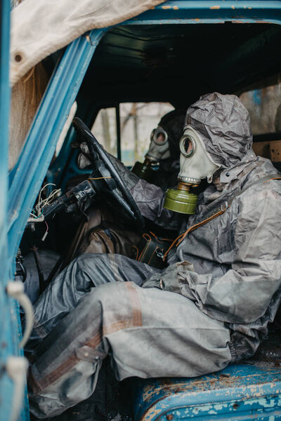 Two persons sits in NBC protective suits and gas masks in old truck. Concept of a preventive measures and protection for coronavirus COVID 19 pandemic and other global dangers.