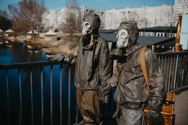 Couple in love walks at bridge and holds hands in NBC protective suits and gas masks. Concept of a preventive measures and protection for coronavirus COVID 19 pandemic and other global dangers.