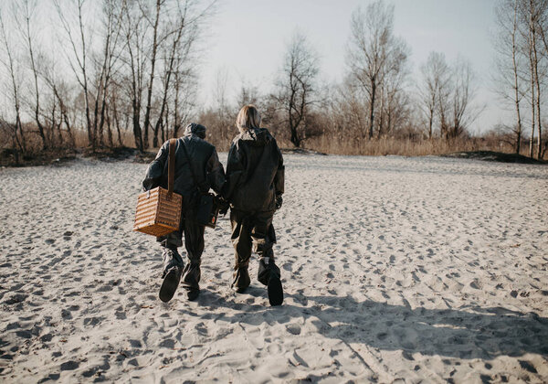 Couple in love walks at beach in NBC protective suits. Concept of a preventive measures and protection for coronavirus COVID 19 pandemic and other global dangers.