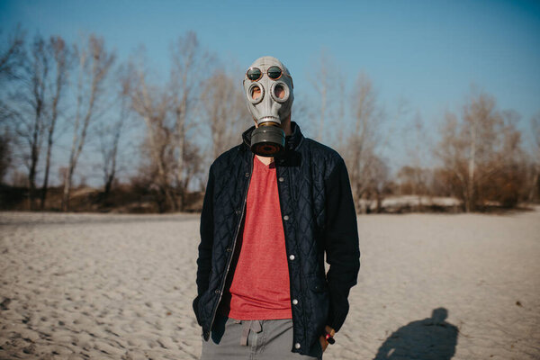 Young man walks in gas mask and sunglasses at beach. Concept of a preventive measures and protection for coronavirus COVID 19 pandemic and other global dangers.