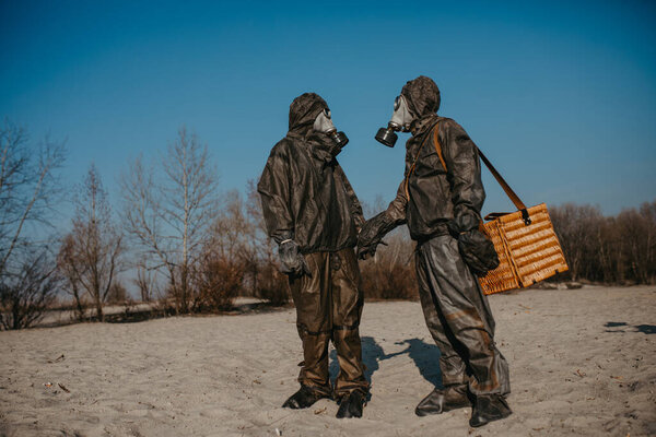 Couple in love walks at beach in NBC protective suits and gas masks. Concept of a preventive measures and protection for coronavirus COVID 19 pandemic and other global dangers.