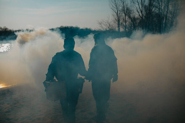 Couple in love walks in NBC protective suits and gas masks on smoke background. Concept of a preventive measures and protection for apocalypse, global pollutions of environment and pandemic.